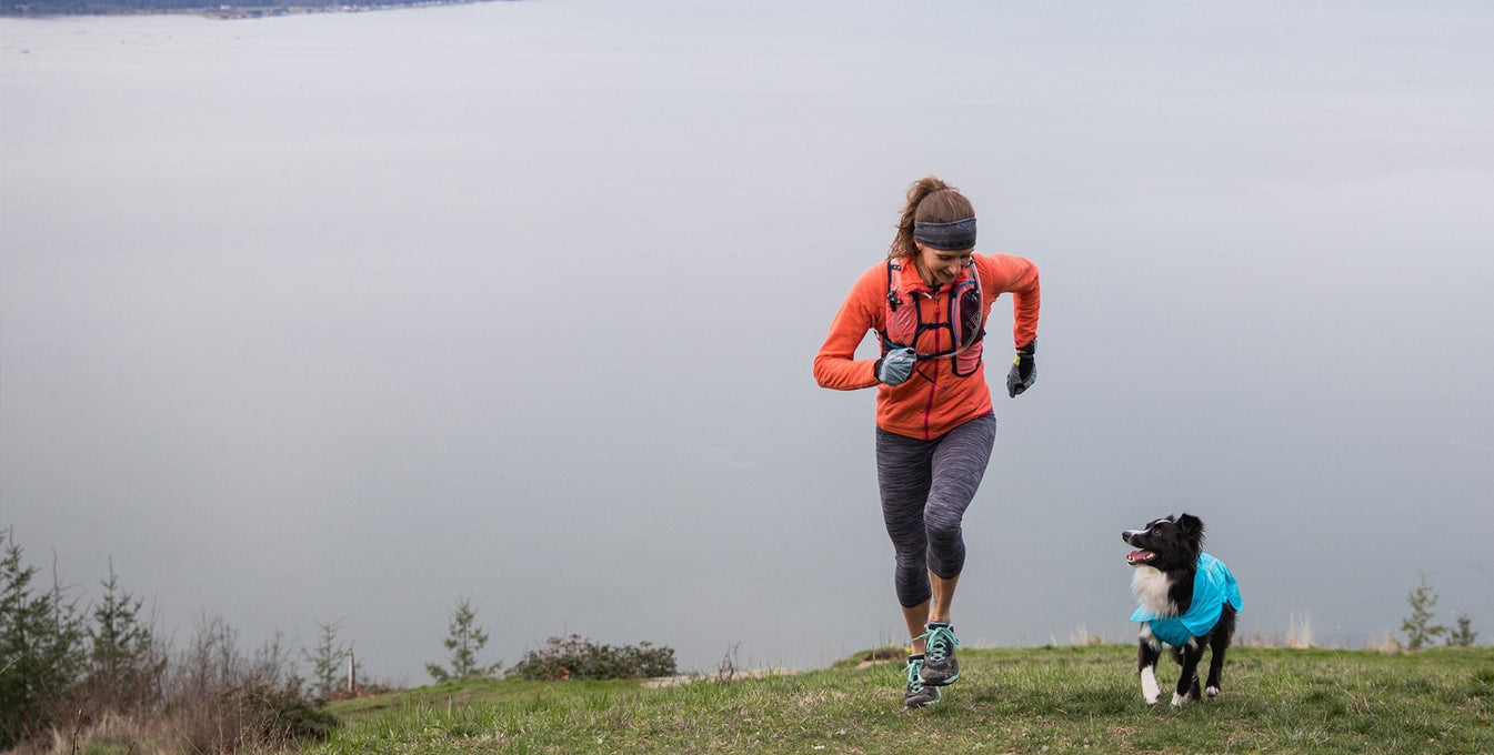 Krissy & PD in Wind Sprinter Jacket run up grassy slope above clouds in the hills.
