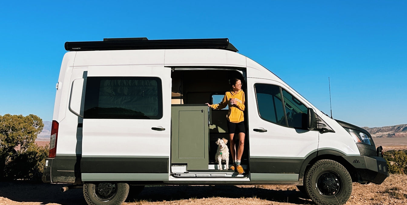 A woman and her dog stand in a camper van. 