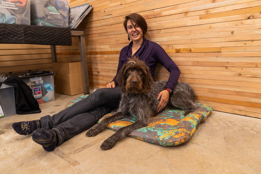 Kadee sits with her dog who is on a dog bed.
