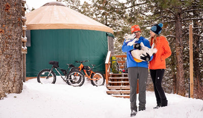 Cade and Becca hold Tala standing in front of a yurt in the snow,