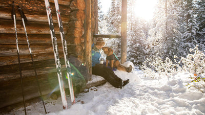 Dog licks humans face while sitting on step of nordic warming hut in the snow.