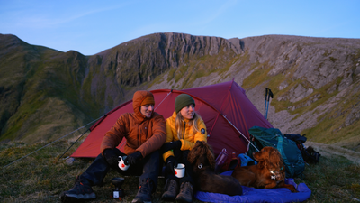 Man and woman and two spaniel dogs sitting in front of a tent in the Scottish Highlands