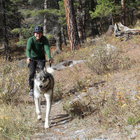 Meg and Leo ride on a trail by the woods together. Leo is a large husky.