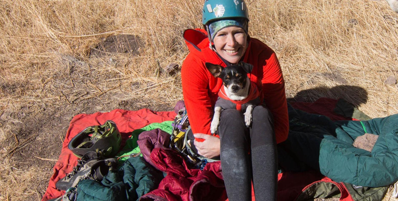 A small dog sits in a woman's lap while they are out in nature. 