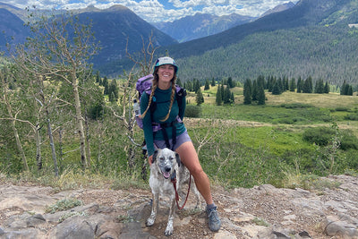 A woman stands with her dog in the mountains in Colorado.