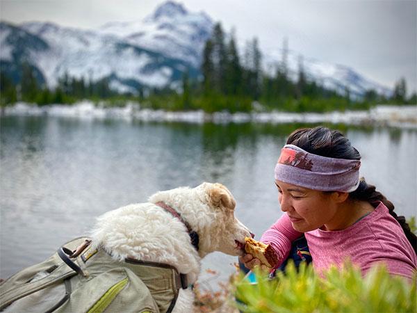 Cassie eats a snack out of Theresa's hands by alpine lake.
