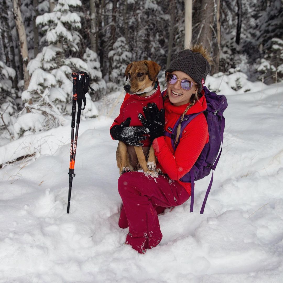 Caroline kneels in skis while holding Lila in her dog puffy in her lap.