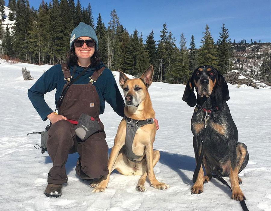 Laura with her two dogs sit on the snow together.