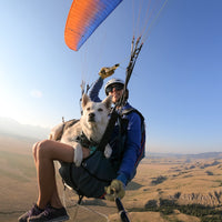 Becca paraglides with her dog Talus, who sits in Ruffwear harness in her lap.