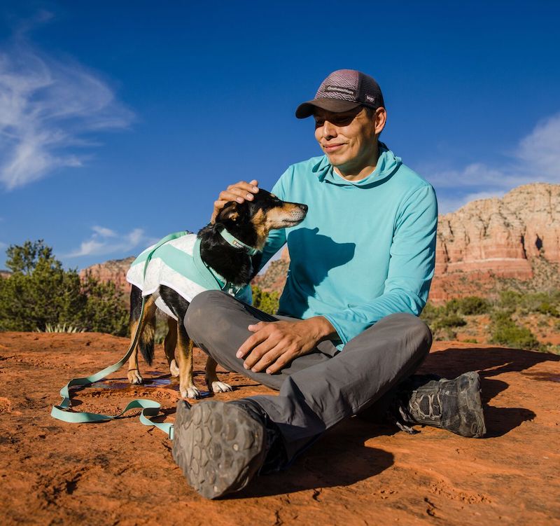 Vernan pets his dog wearing a cooling jacket in the desert.