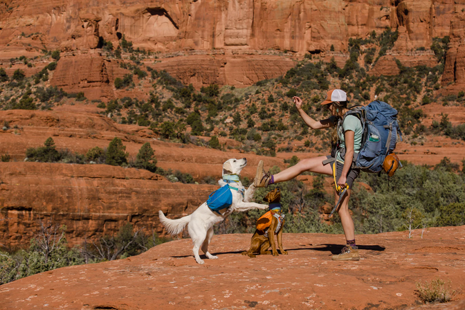Hailey kicks in the air in joy while her two dogs jump next to her on a desert backpacking trip.